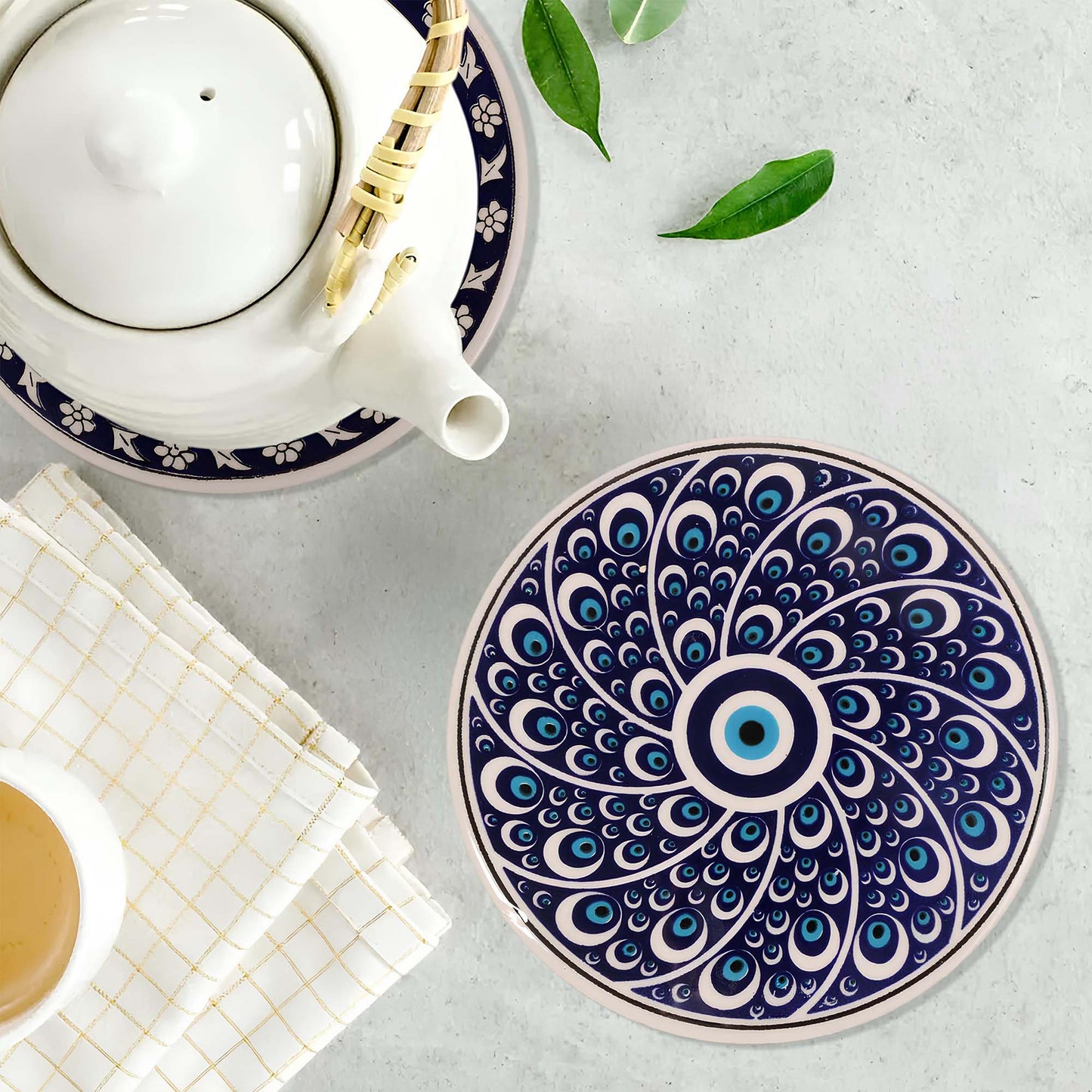 Decorative blue and white peacock feather trivet on a light gray surface with a teapot and cup.