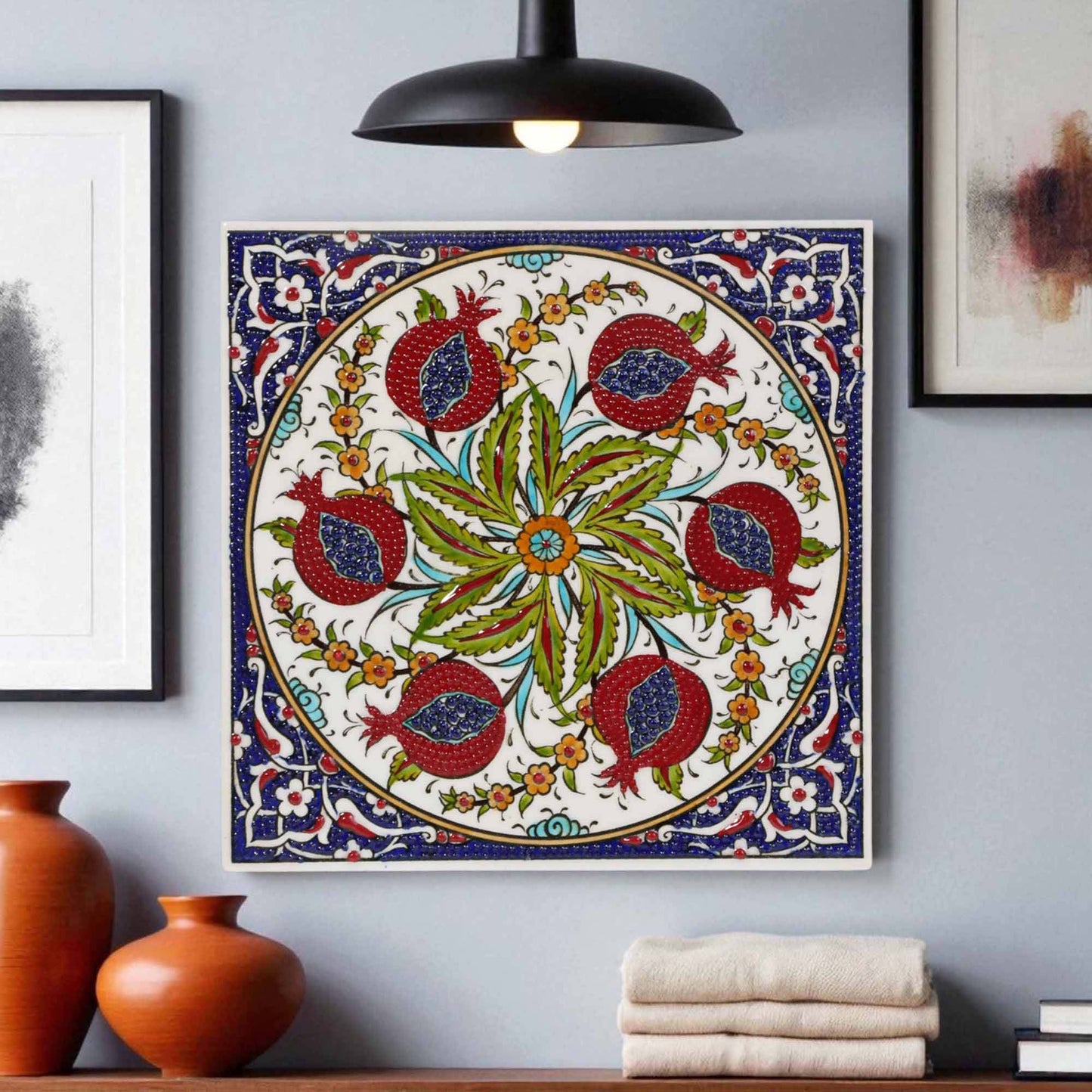 Decorative ceramic tile with floral and pomegranate design on a wall with vases and books below.