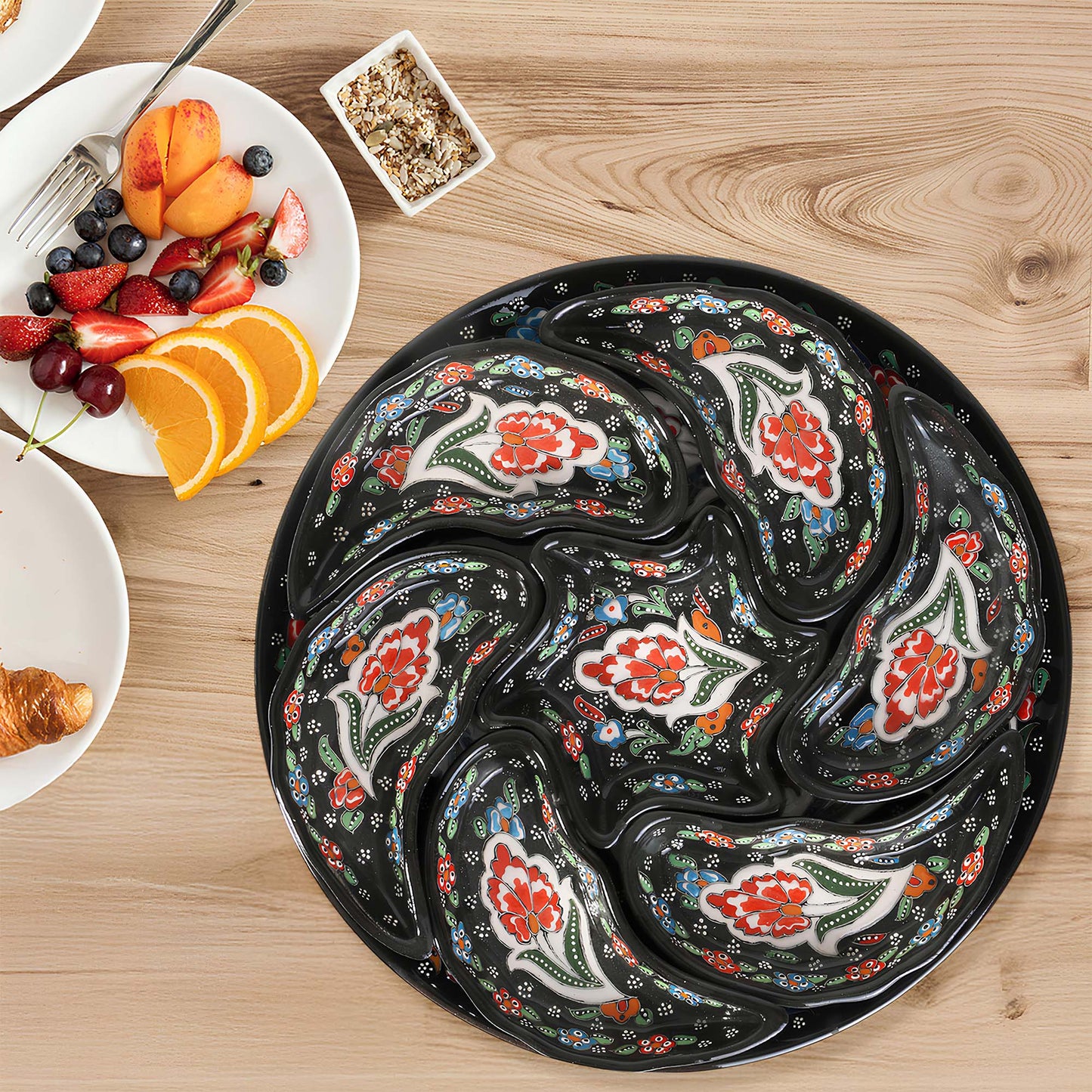 Decorative black snack serving trays set with floral patterns on a wooden table with a fruit and pastry set.
