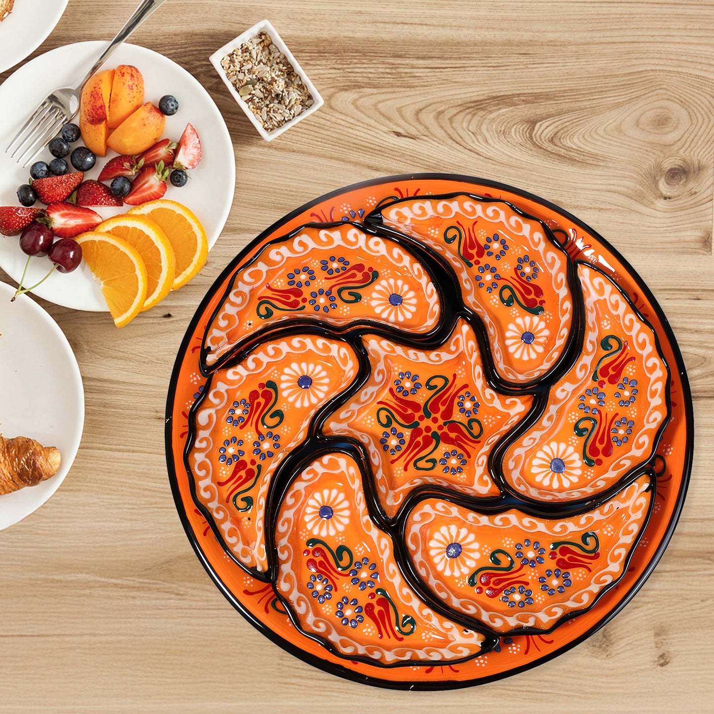 Decorative snack serving tray set with intricate designs on a wooden table with fruit and pastries.