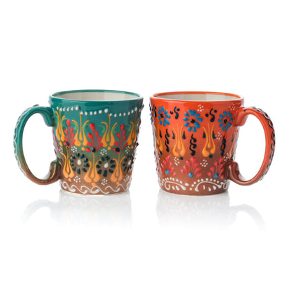 Two handcrafted ceramic coffee mugs, one in moss green and the other in orange, both with floral and geometric patterns.