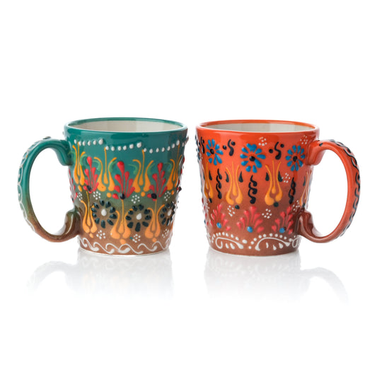 Two handcrafted ceramic coffee mugs, one in moss green and the other in orange, both with floral and geometric patterns.