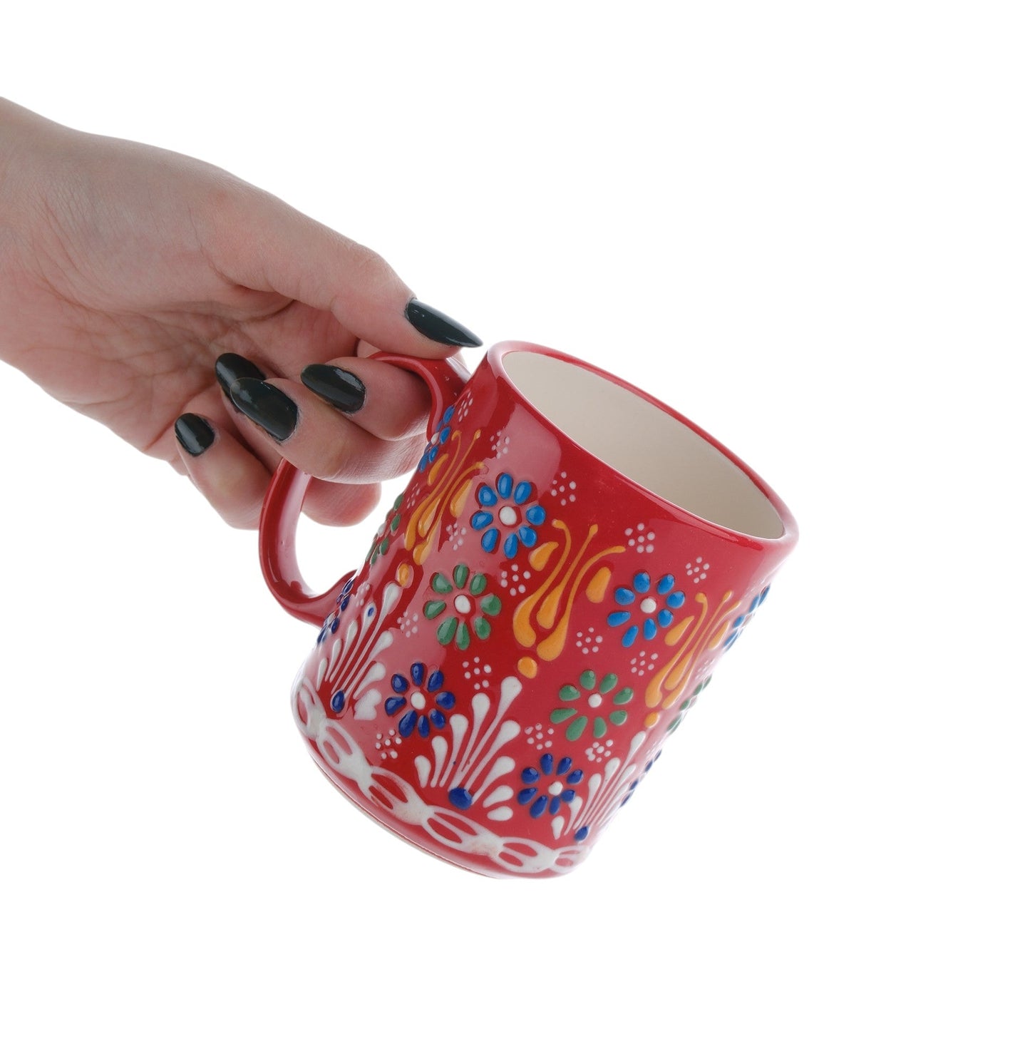 A hand holding a colorful handcrafted ceramic coffee mug with floral patterns.