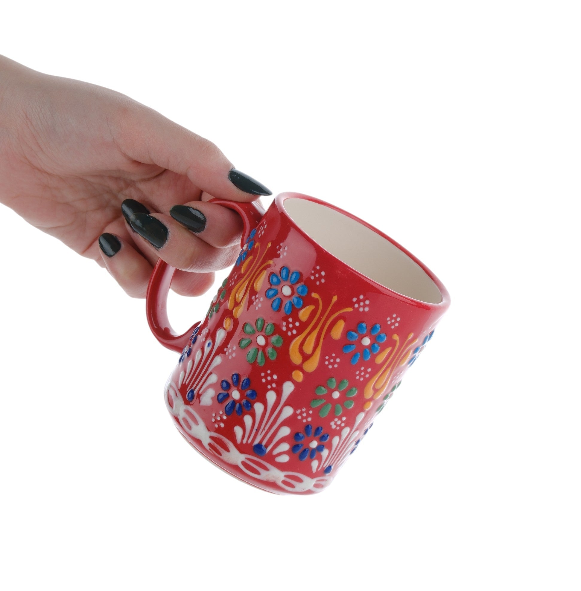 A hand holding a colorful handcrafted ceramic coffee mug with floral patterns.