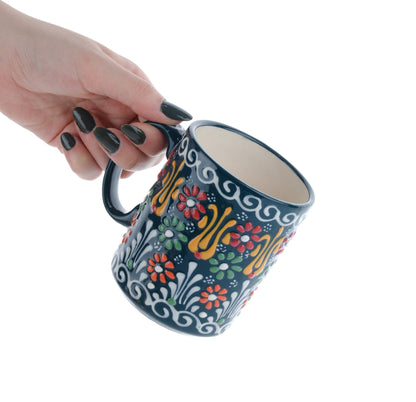 A hand holding a colorful handcrafted ceramic coffee mug with floral patterns.