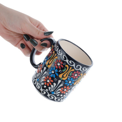 A hand holding a colorful handcrafted ceramic coffee mug with floral patterns.