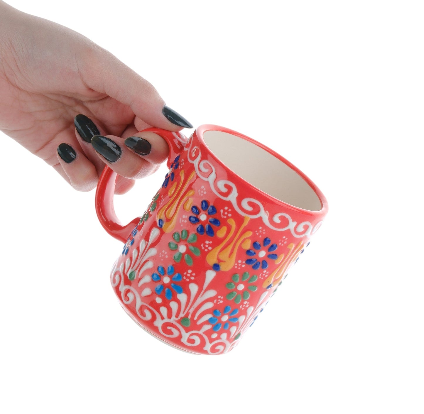 A hand holding a colorful handcrafted ceramic coffee mug with floral patterns.