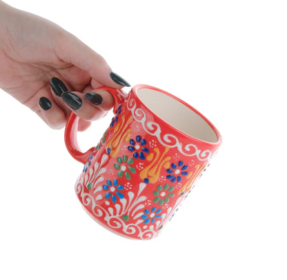 A hand holding a colorful handcrafted ceramic coffee mug with floral patterns.