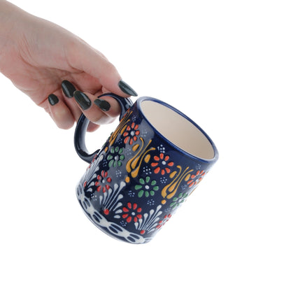 A hand holding a colorful handcrafted ceramic coffee mug with floral patterns.