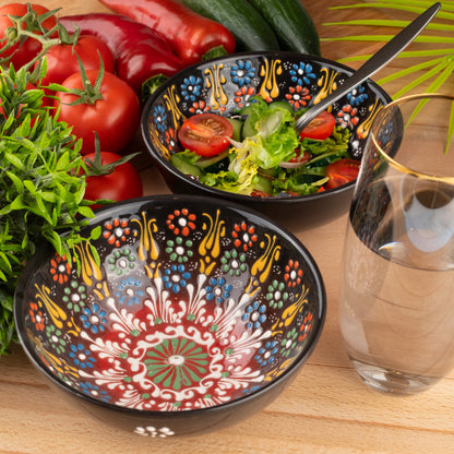 Decorative salad bowls with floral patterns containing salad and tomatoes, next to a glass of water on a wooden surface.