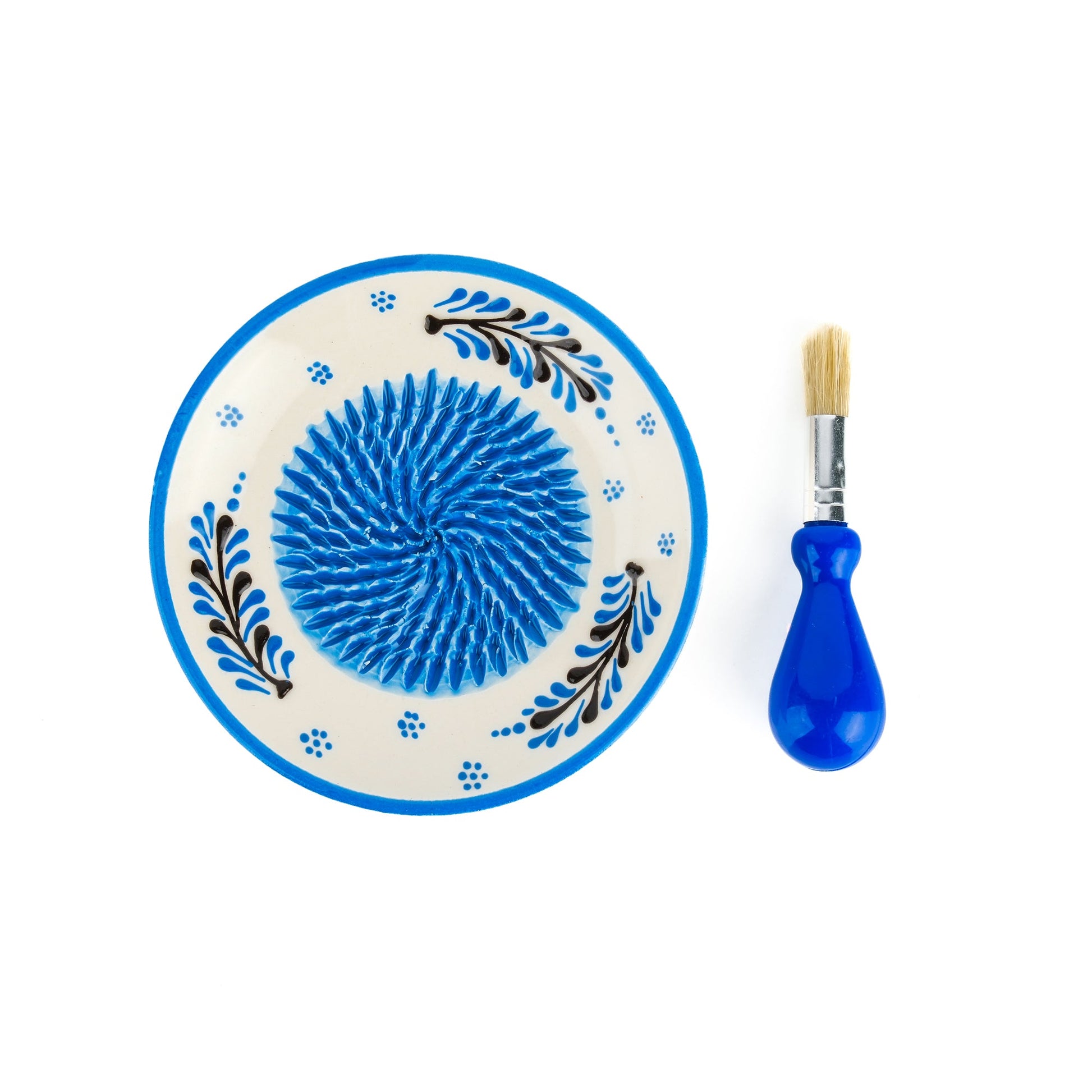 Decorative ceramic garlic grater plate with blue center and floral patterns, accompanied by a blue-handled brush on a white background.