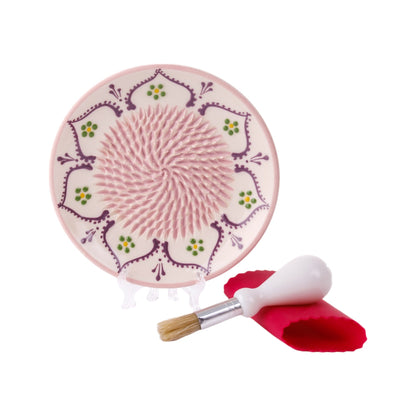 A ceramic garlic grater plate in vanilla white color with a decorative pattern, accompanied by a silicone peeler and cleaning brush.