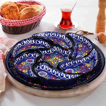 Decorative ceramic snack serving tray set with floral patterns on a white surface, accompanied by a basket of bread and a glass of tea.