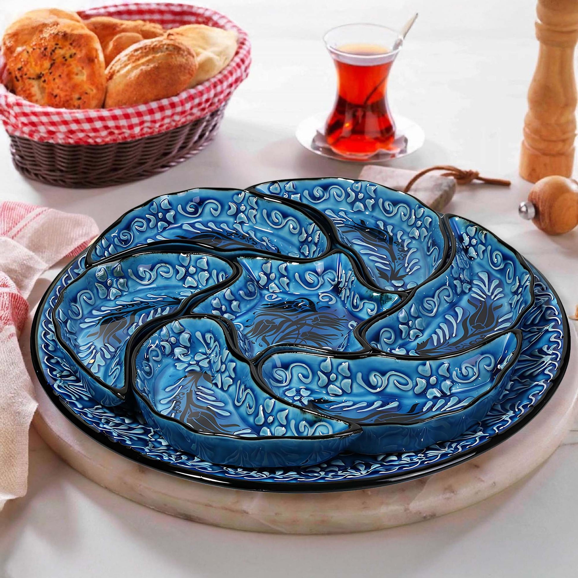 Blue ceramic snack serving tray set with intricate designs on a white surface, accompanied by a basket of bread and a glass of tea.