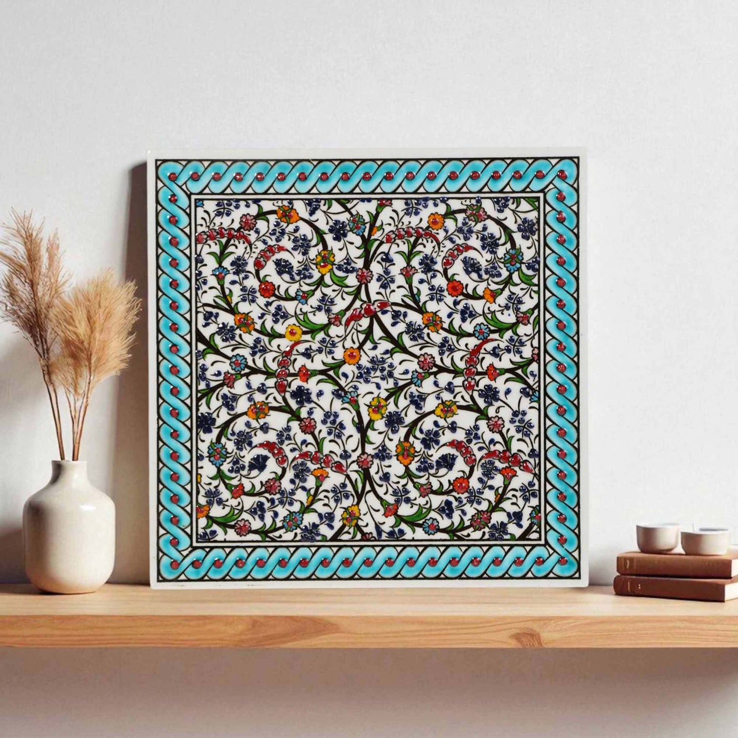 Decorative ceramic tile wall art with floral pattern on a wooden shelf