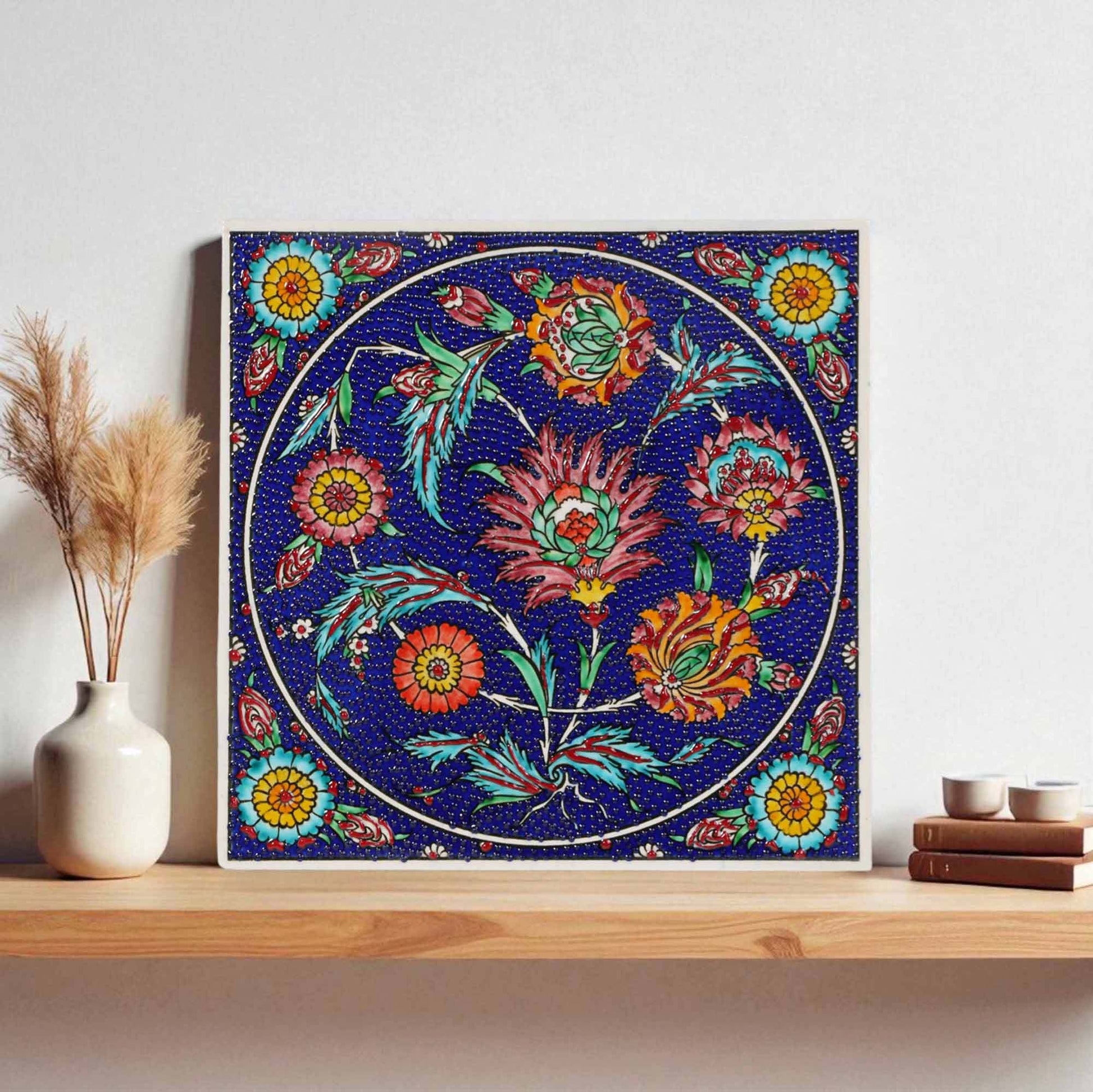 Decorative floral ceramic tile on a blue background with a white frame, placed on a wooden surface.