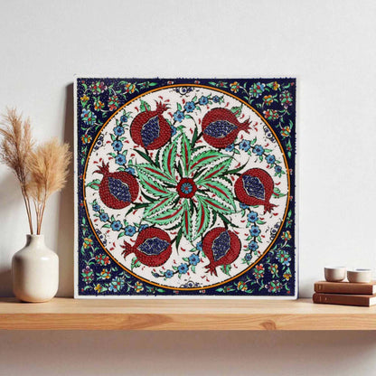 Decorative ceramic tile with floral and pomegranate design on a wooden shelf.