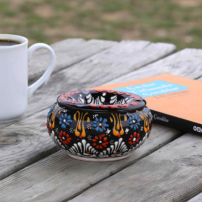 Decorative ceramic ashtray with floral patterns on a wooden surface next to a white mug.