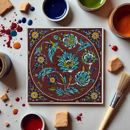 Decorative ceramic tile with floral pattern surrounded by paint containers and a brush on a light background