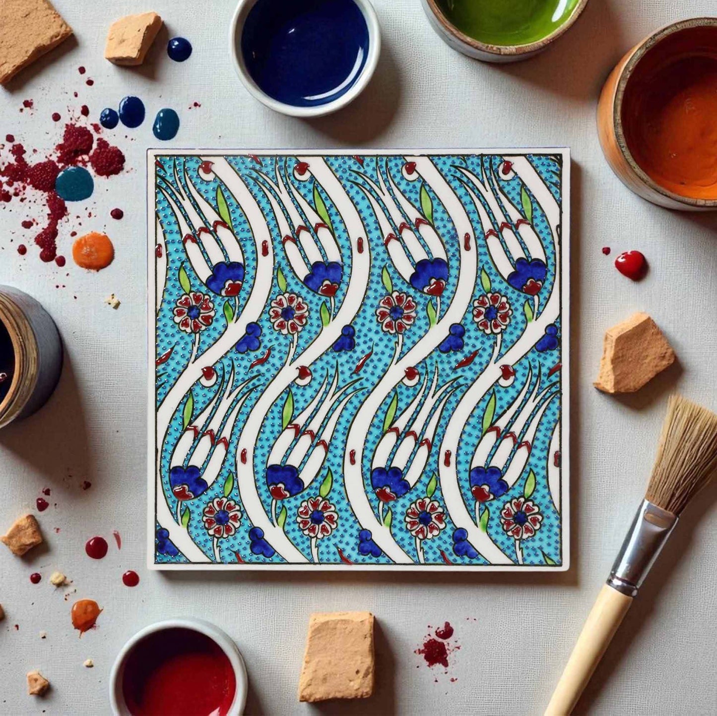 Decorative ceramic tile with floral pattern surrounded by paint containers and a brush on a light background