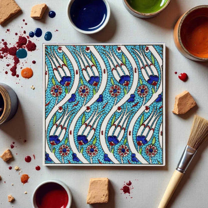 Decorative ceramic tile with floral pattern surrounded by paint containers and a brush on a light background