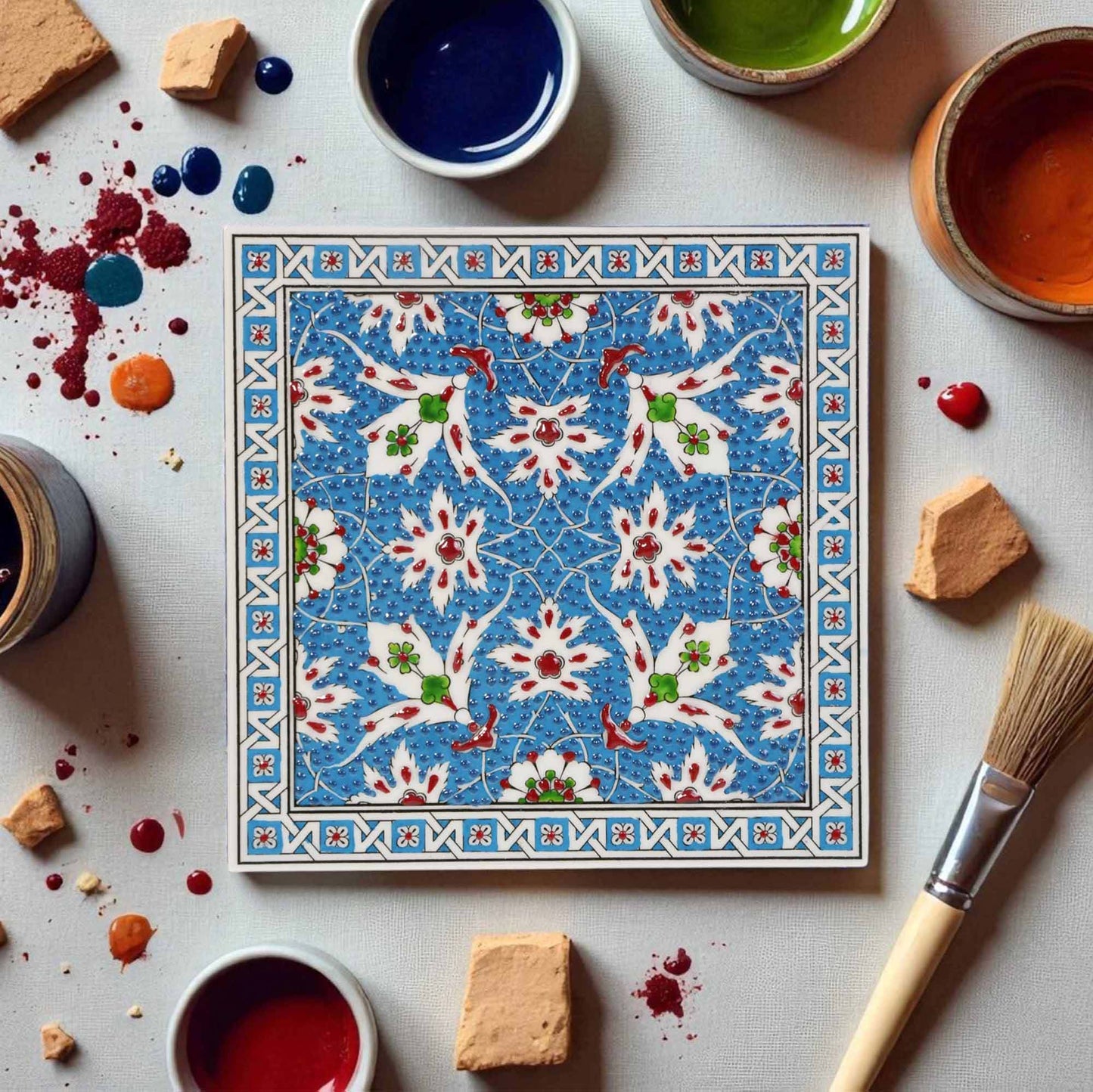 Decorative ceramic tile with floral pattern surrounded by painting supplies on a light gray background