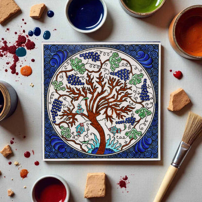 Colorful ceramic tile with a tree design surrounded by paint containers and tools on a light surface.