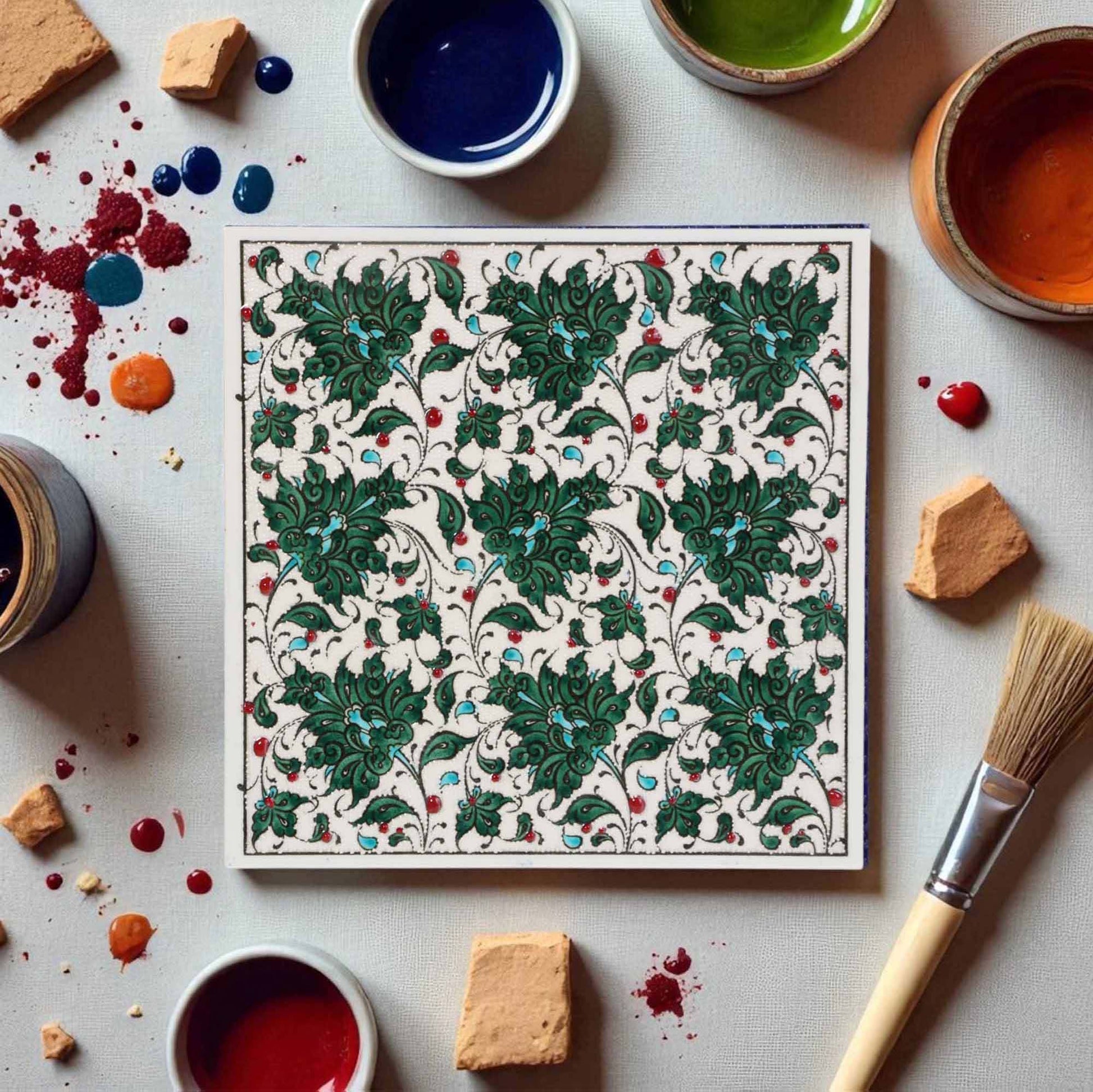 Decorative ceramic tile with intricate green pattern on a table with paint containers and tools