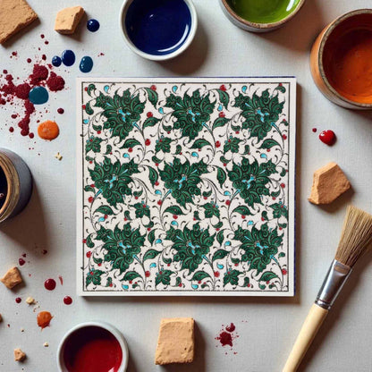 Decorative ceramic tile with intricate green pattern on a table with paint containers and tools