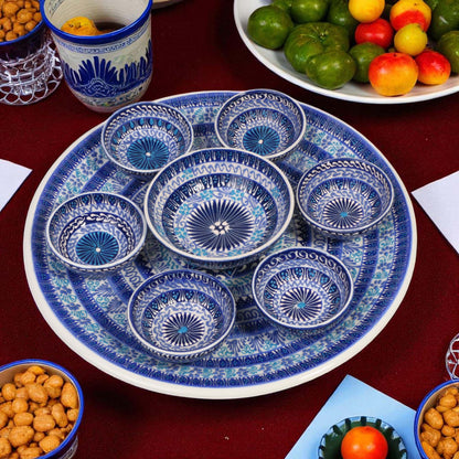 Set of blue and white ceramic dishes on a table with snacks and fruits.