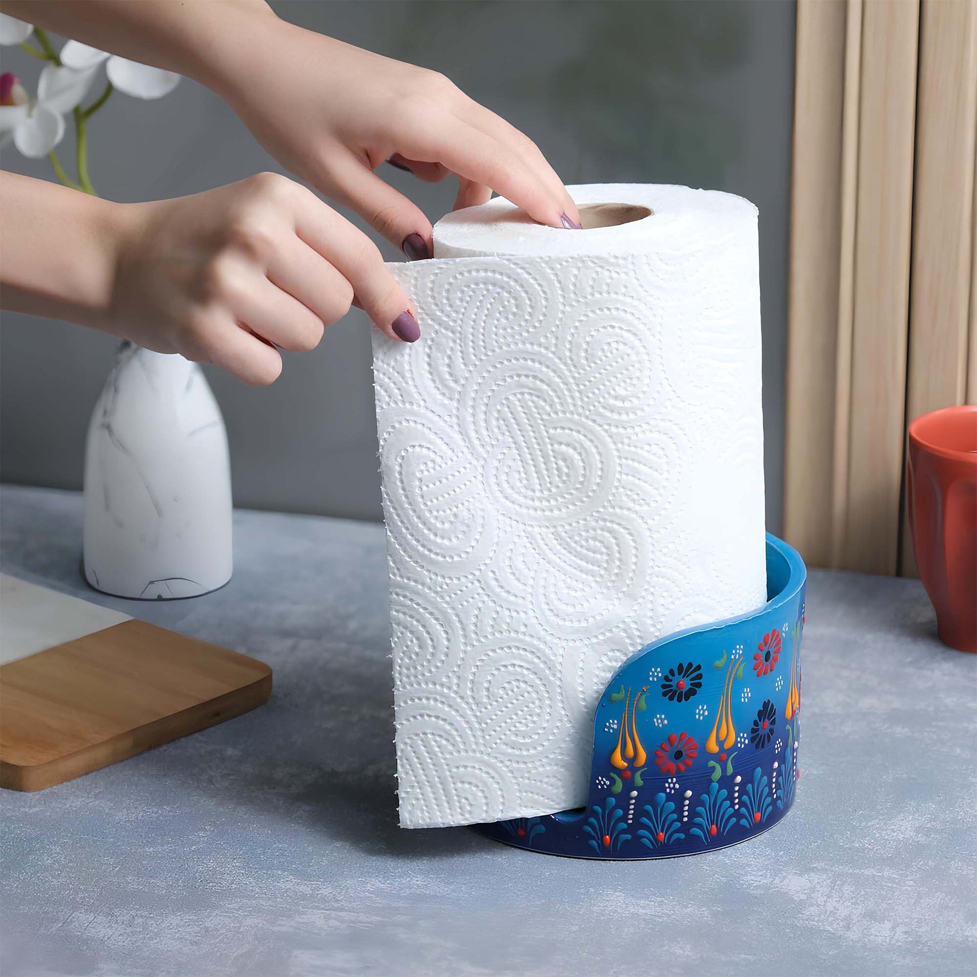 Person reaching for a roll of paper towels on a decorative paper towel holder with a floral design.