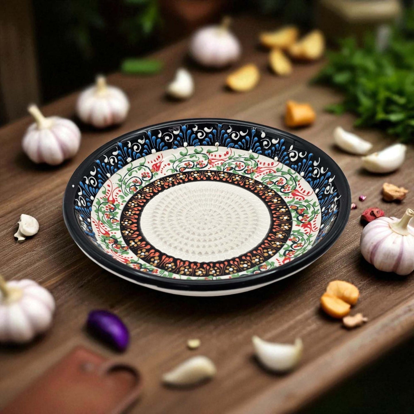 Decorative ceramic garlic grater bowl with intricate patterns on a wooden surface with garlic and herbs.