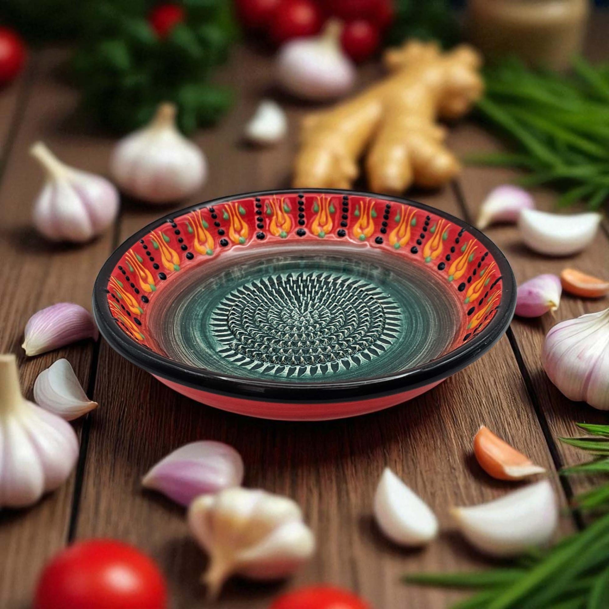 Decorative ceramic garlic grater bowl with a flame pattern on a wooden surface with garlic and tomatoes.