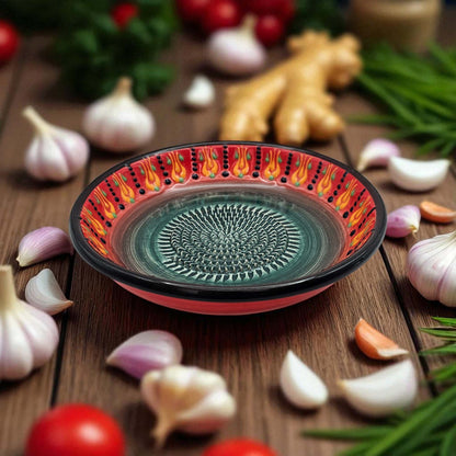 Decorative ceramic garlic grater bowl with a flame pattern on a wooden surface with garlic and tomatoes.