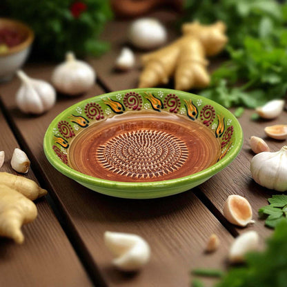 Decorative ceramic garlic grater bowl with a green rim on a wooden surface with garlic and ginger.