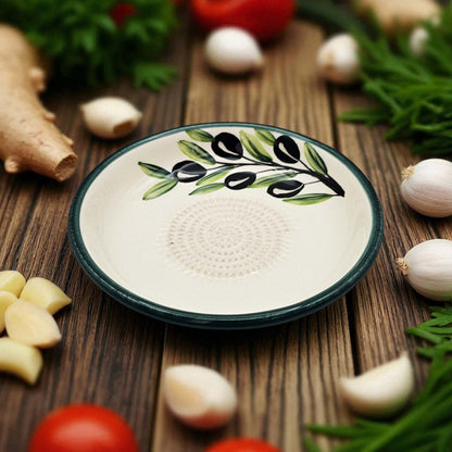 Ceramic garlic grater bowl with olive design on a wooden surface with vegetables