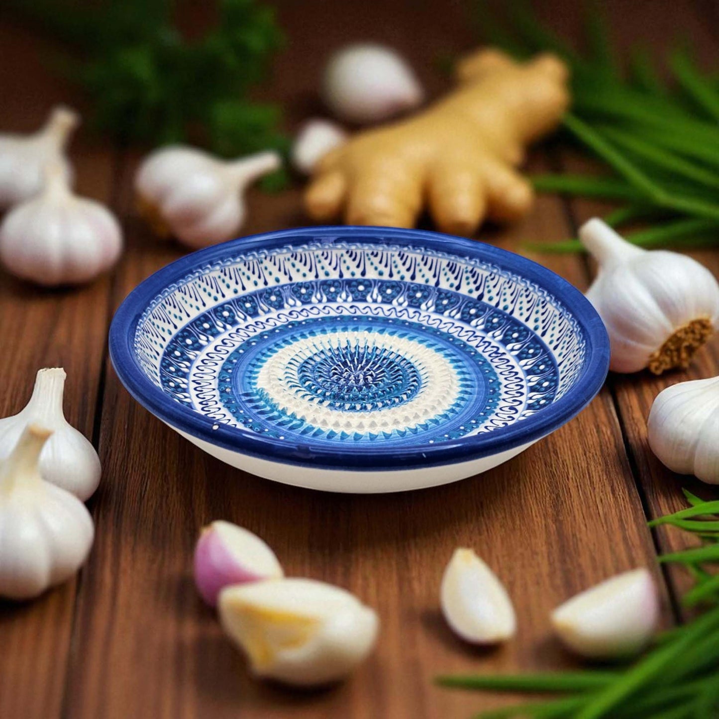 Decorative ceramic garlic grater bowl with blue and white pattern on a wooden surface with garlic and ginger.