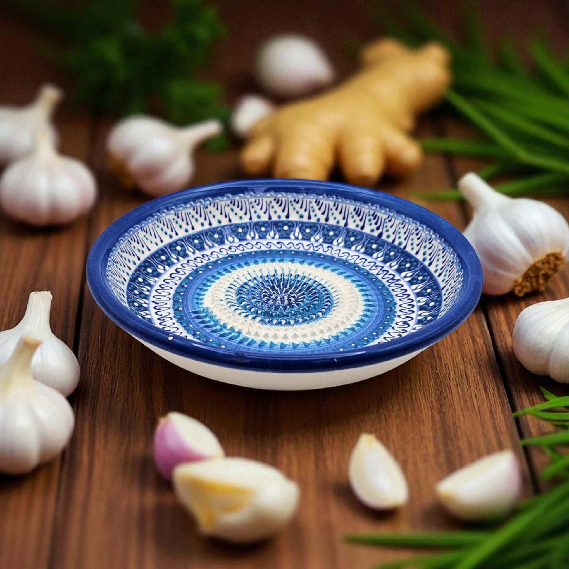 Decorative ceramic garlic grater bowl with blue and white pattern on a wooden surface with garlic and ginger.