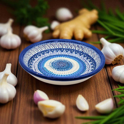 Decorative ceramic garlic grater bowl with blue and white pattern on a wooden surface with garlic and ginger.