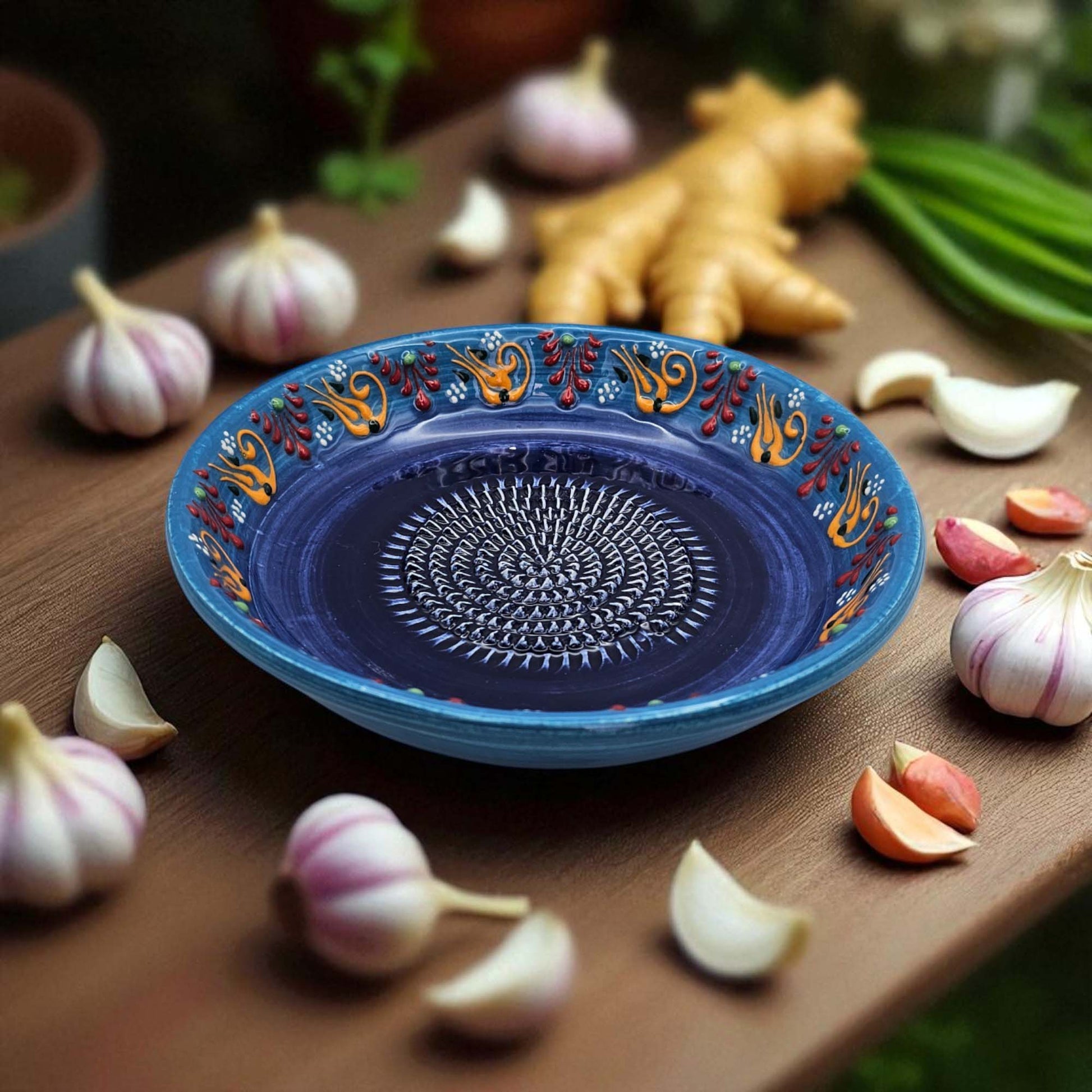 Decorative blue garlic grater bowl with floral patterns on a wooden surface with garlic and ginger.