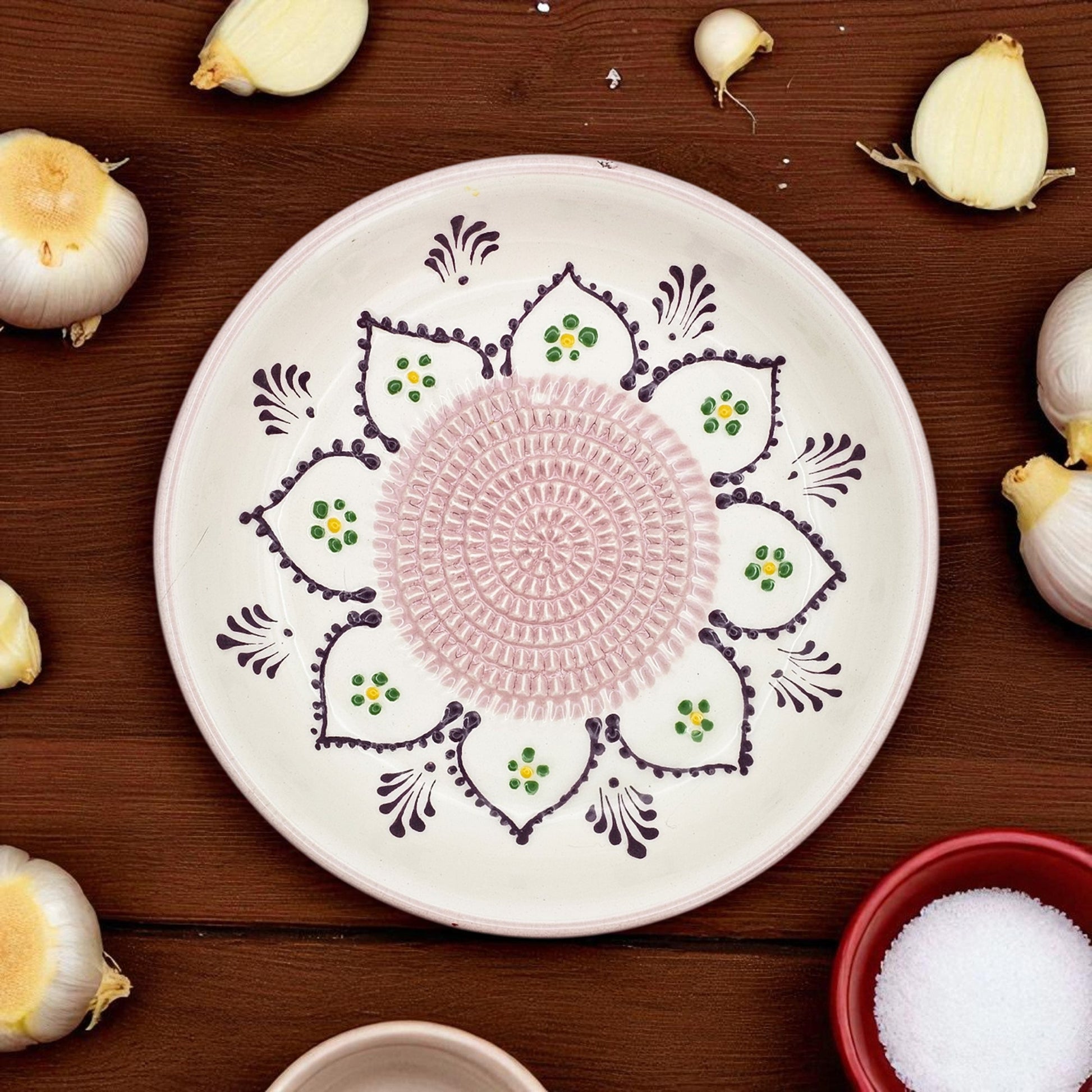 Decorative garlic grater bowl with intricate patterns on a wooden surface with garlic bulbs.