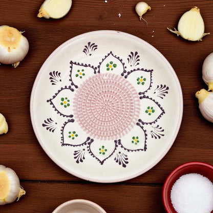Decorative garlic grater bowl with intricate patterns on a wooden surface with garlic bulbs.