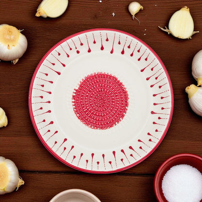 Decorative garlic grater bowl with red patterns on a wooden surface with garlic bulbs