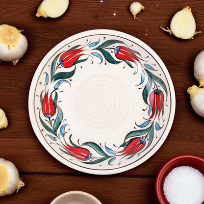 Decorative ceramic garlic grater bowl with floral design on a wooden surface with garlic bulbs.