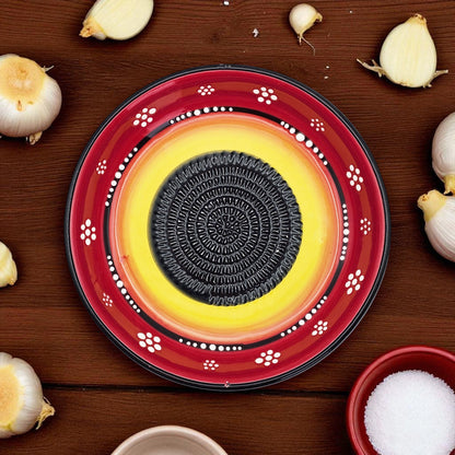 Decorative garlic grater bowl with a central circular design on a wooden surface with garlic bulbs.