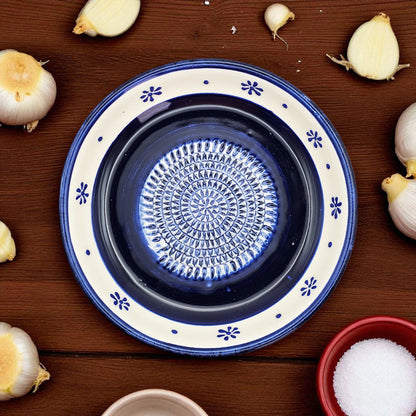 Blue ceramic garlic grater bowl with white rim on a wooden surface with garlic bulbs