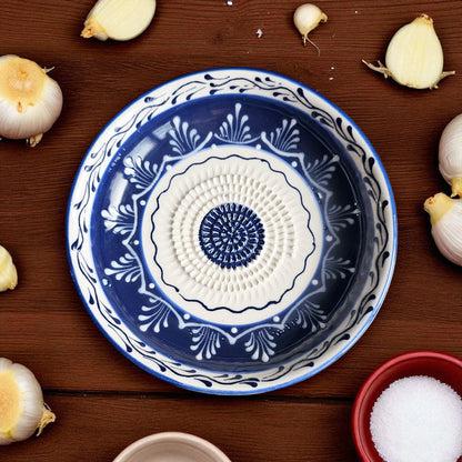 Decorative blue and white garlic grater bowl on a wooden surface with garlic bulbs and a bowl of salt.