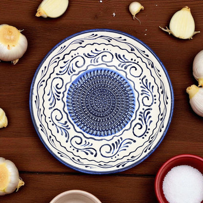 Decorative ceramic garlic grater bowl with blue and white patterns on a wooden surface with garlic bulbs.