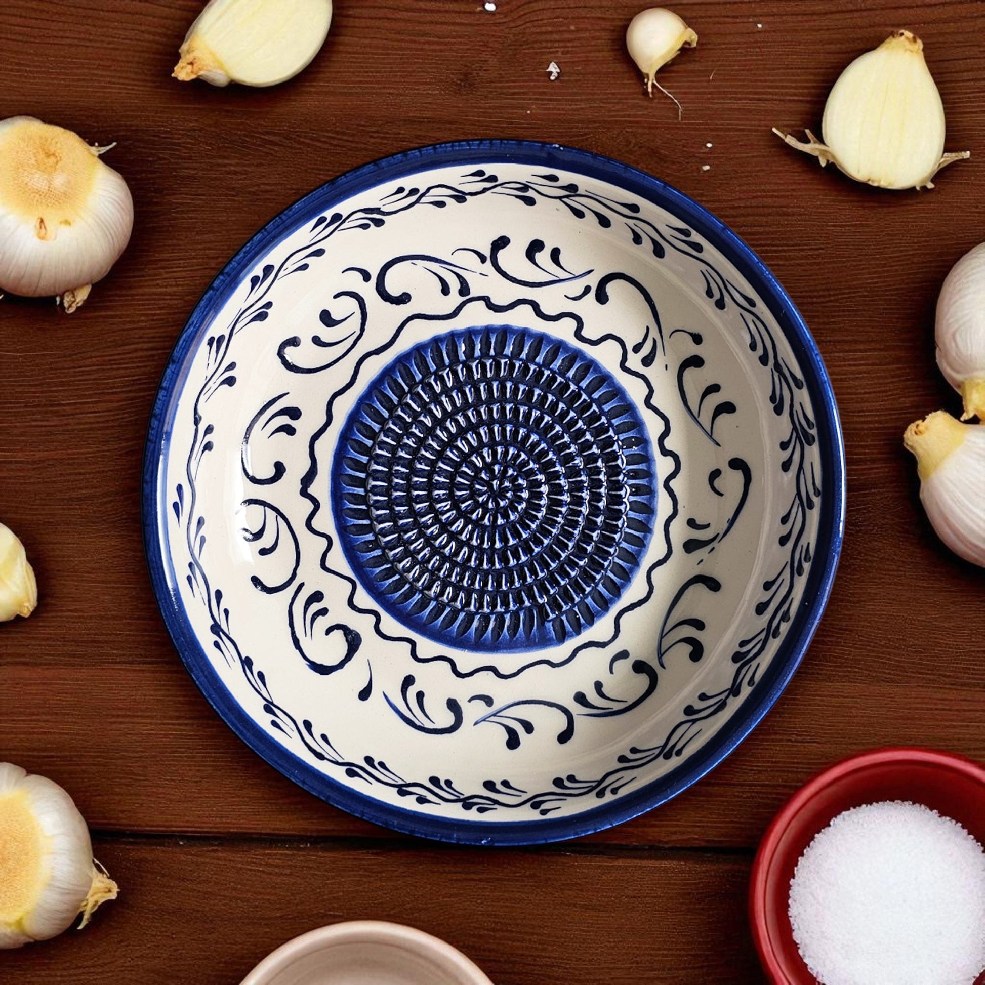 Decorative ceramic garlic grater bowl with blue and white patterns on a wooden surface with garlic bulbs.