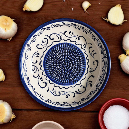 Decorative ceramic garlic grater bowl with blue and white patterns on a wooden surface with garlic bulbs.